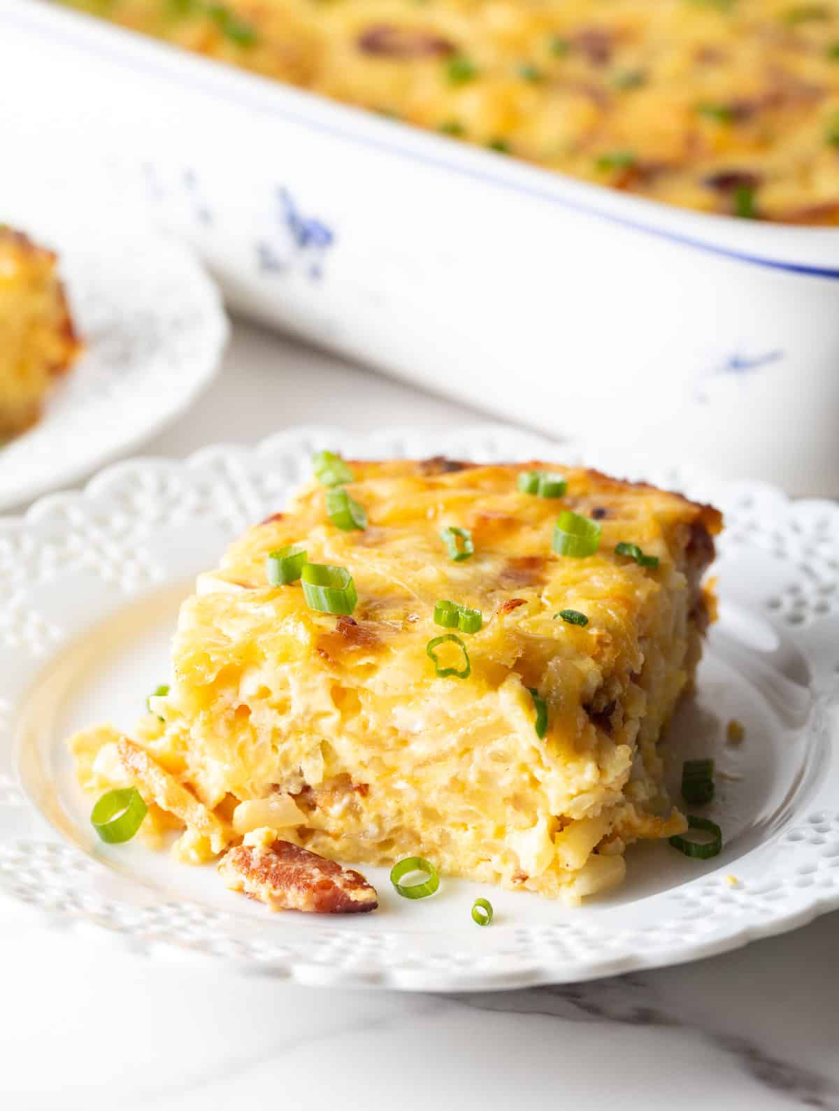 Square serving of hash brown potato, egg and cheese casserole on a white plate.