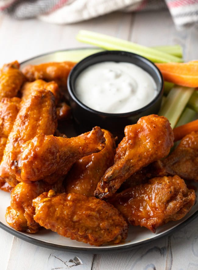 Plateful of baked buffalo chicken wings with black ramekin of ranch dressing, carrot sticks and celery sticks.