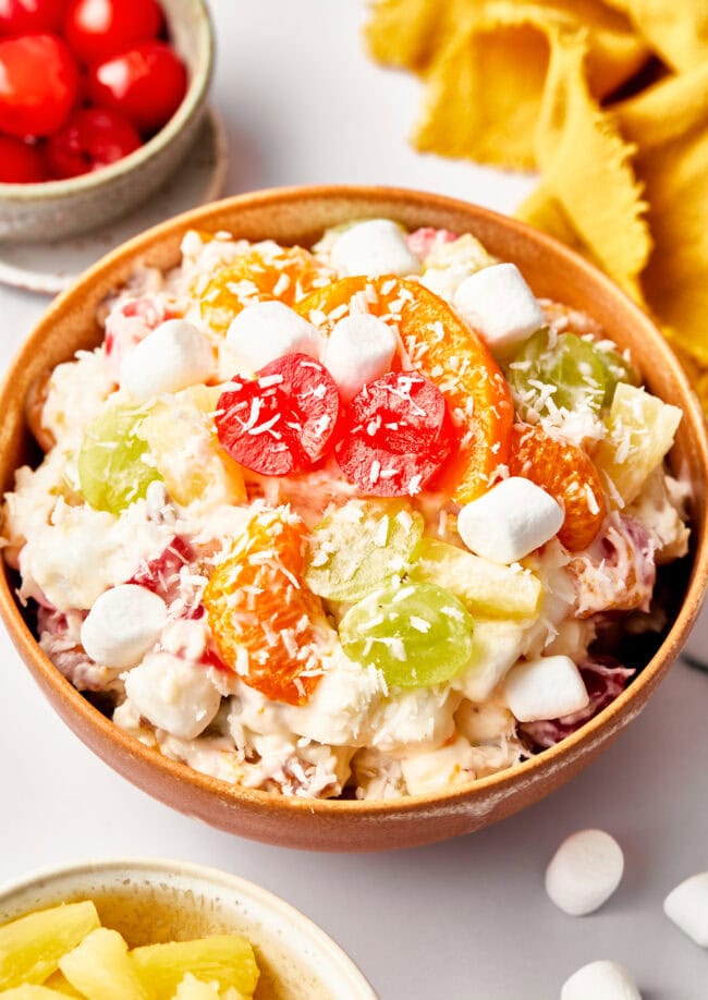 An overhead view of the ambrosia salad in a bowl. Ingredients include marshmallows, cherries, grapes.  