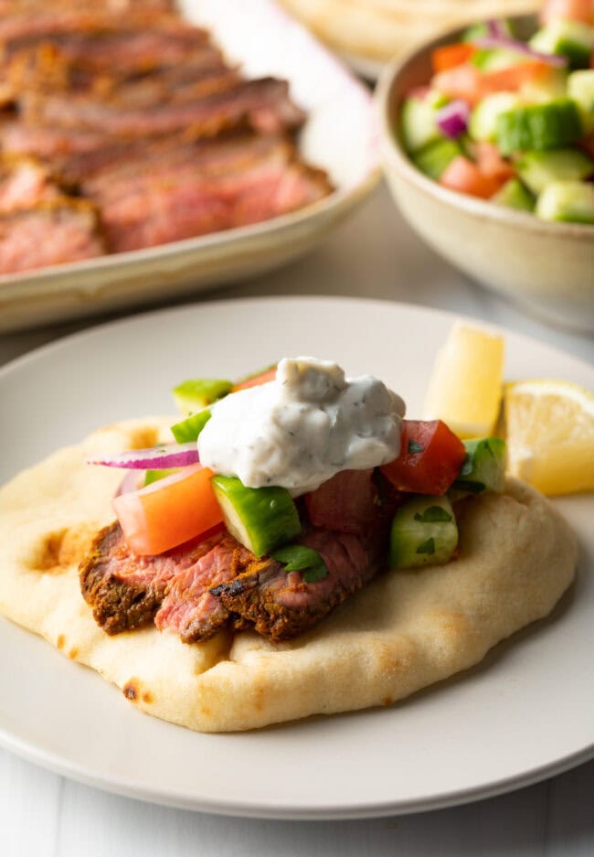 Close view flatbread naan beef shawarma wrap topped with chopped cucumbers, tomatoes, red onion and tzatziki sauce.