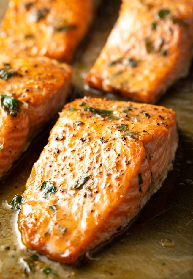 Broiled salmon filets with garlic herb butter on parchment.