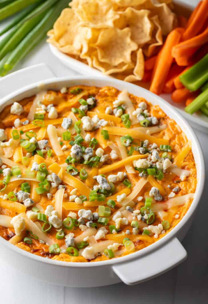 Baked buffalo chicken dip in a large white round dish, topped with green onions.