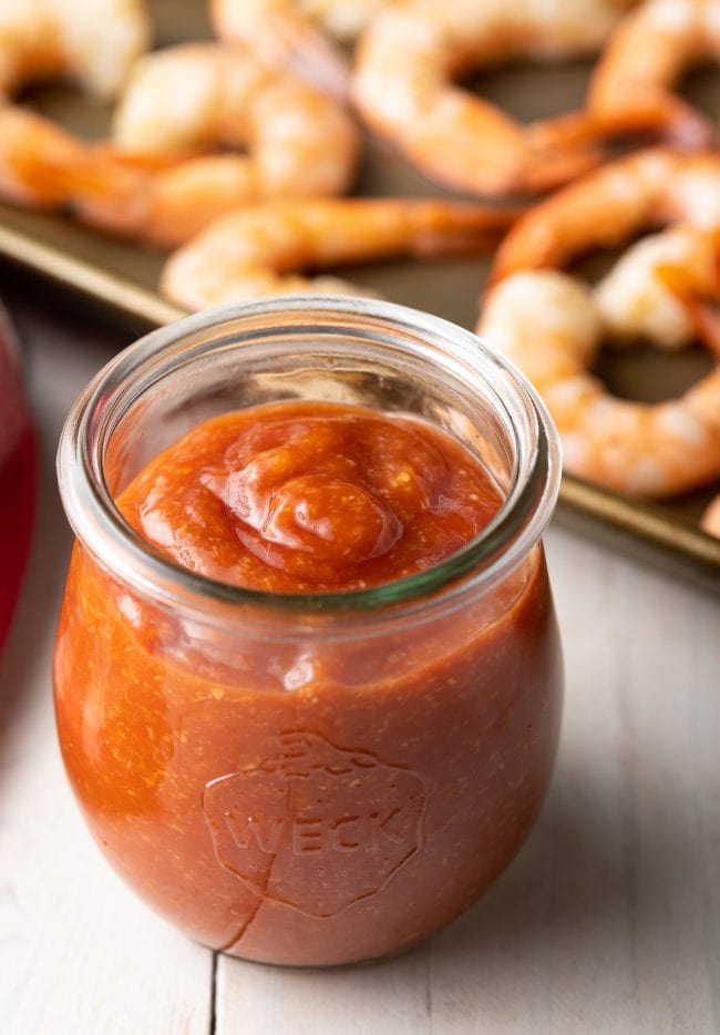 Small jar of homemade cocktail sauce  recipe with shrimp in the background. 