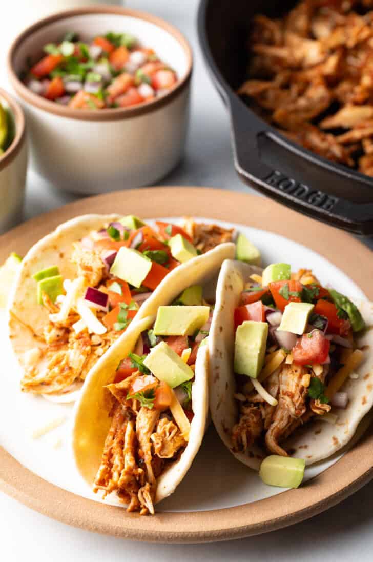 Three chicken tacos with chopped avocado on a plate together.