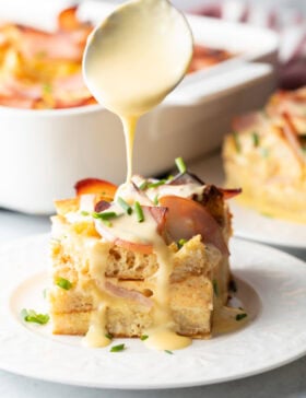 Slice of eggs benedict casserole with hollandaise being drizzled over it with a spoon.