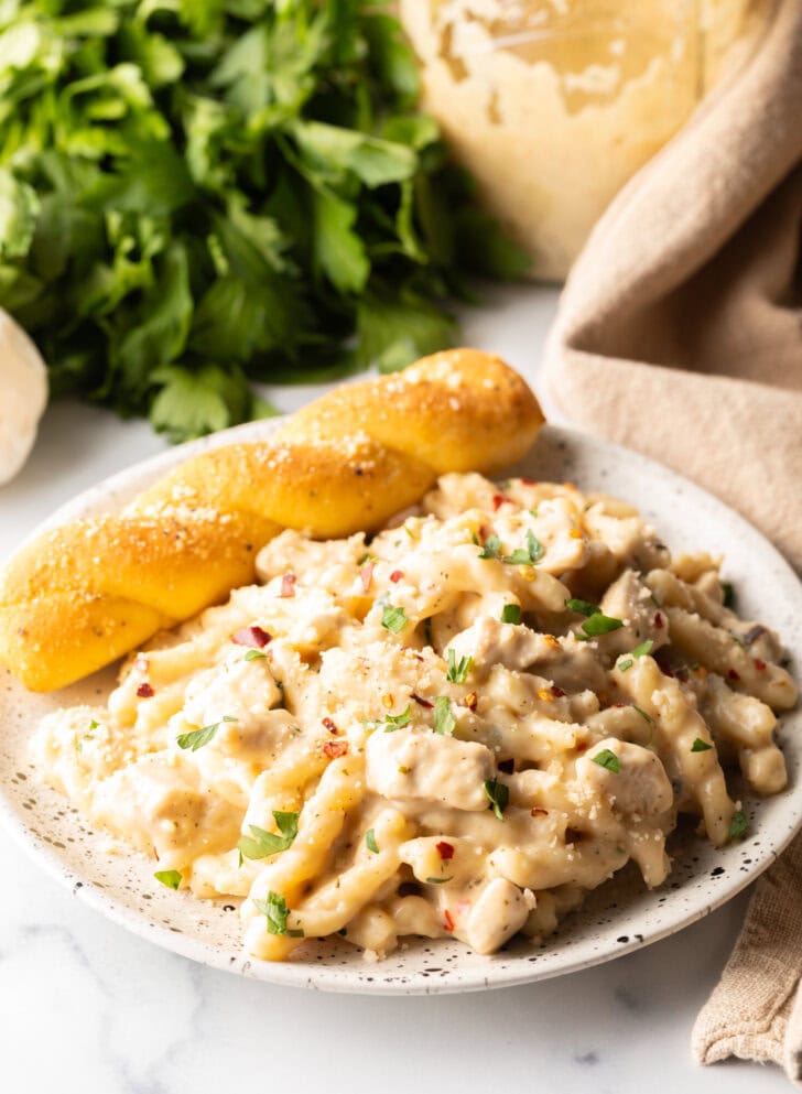 White plate of cheesy garlic parmesan chicken pasta with a breadstick twist on the side of the plate