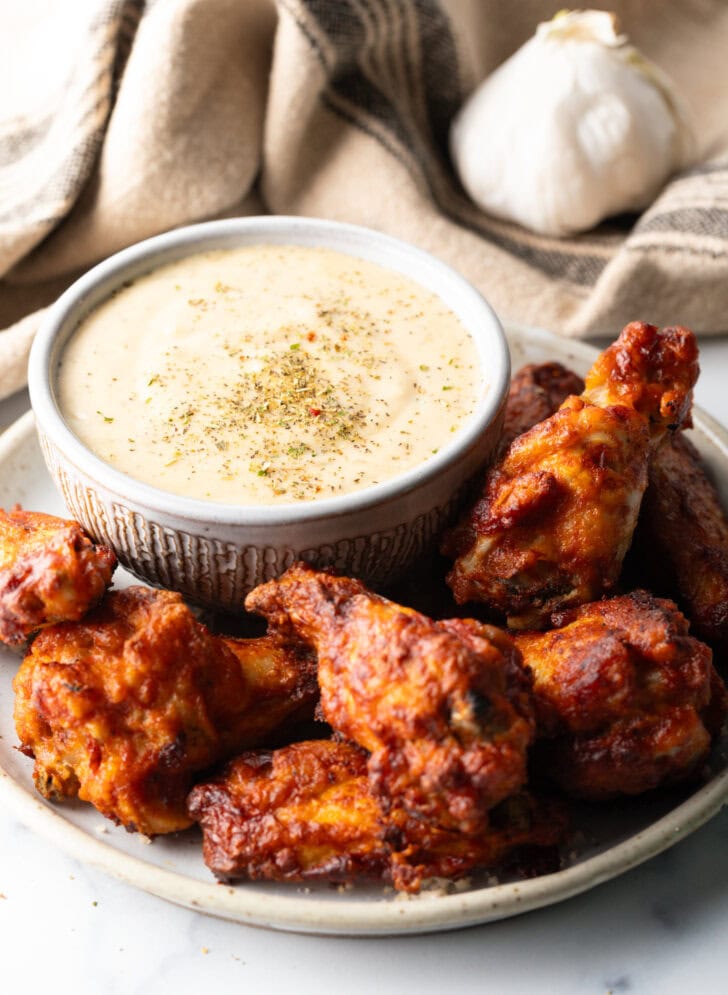 Plate of chicken wings with ramekin of garlic parmesan sauce.