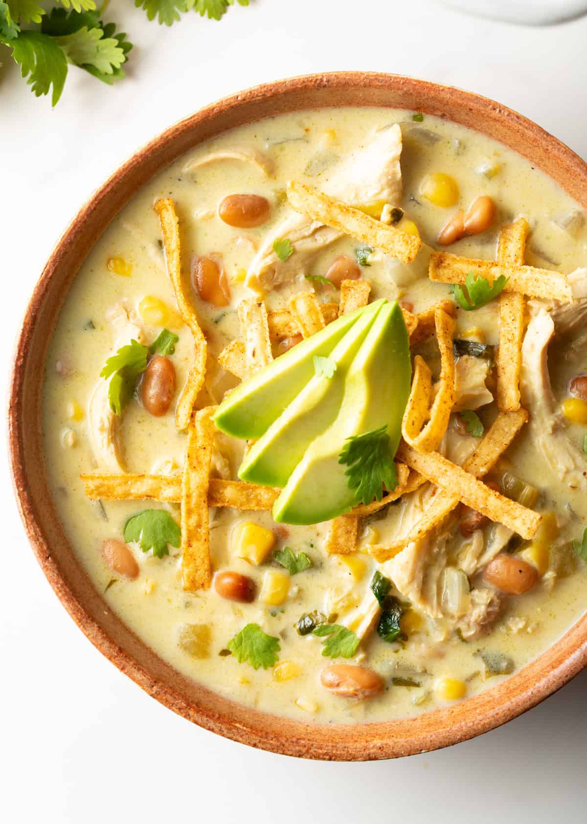 Top down view bowl of green chicken enchilada soup, topped with tortilla strips and slices of avocado.