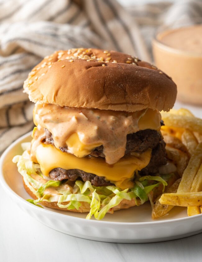 Double patty stacked cheeseburger with homemade Big Mac sauce next to a serving of french fries on a white plate.