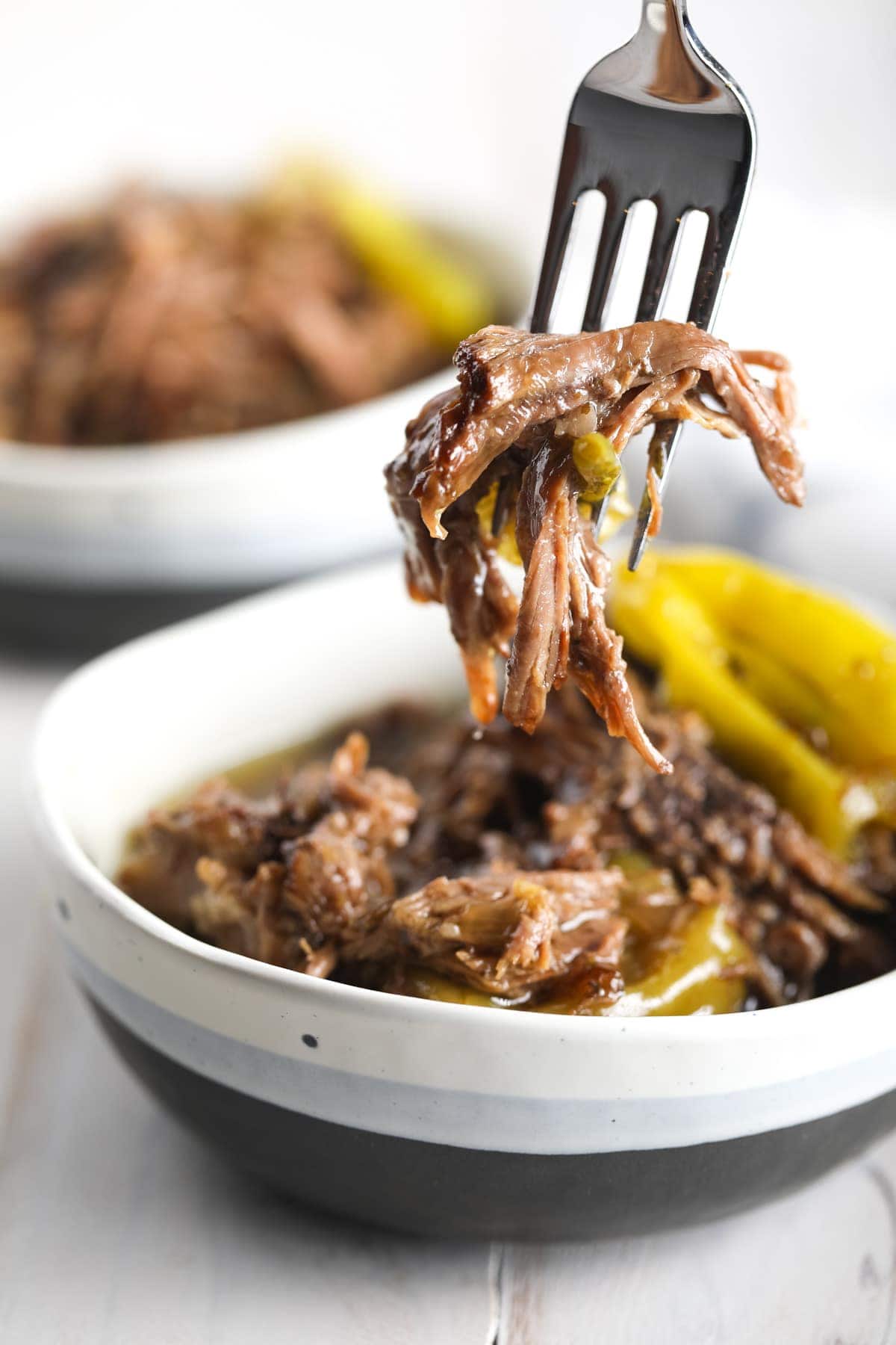 Shredded Italian beef in a bowl with a fork taking a bite or shredded beef. 
