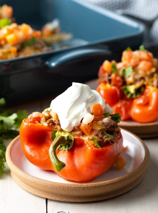 keto taco stuffed peppers on small white plate with toppings over pepper