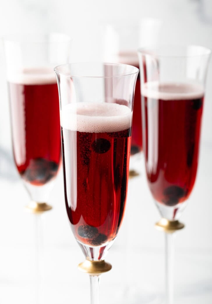 Four fluted glasses with deep red kir royale cocktail drinks.