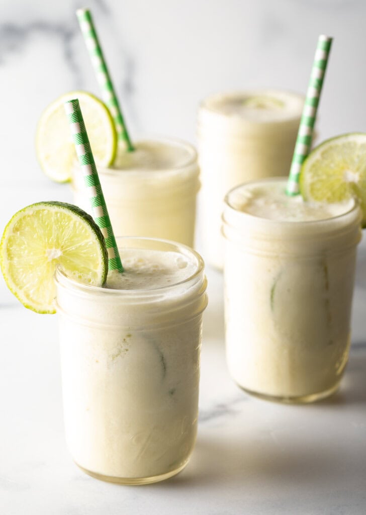 four glasses of Brazilian limeade, each garnished with a slice of lime and a green and white striped straw