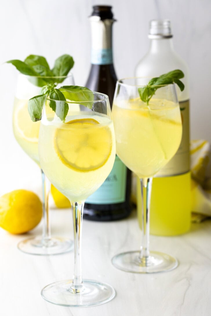 3 wine glasses each with limoncello spritz, fresh slices of lemon, and fresh mint leaves.