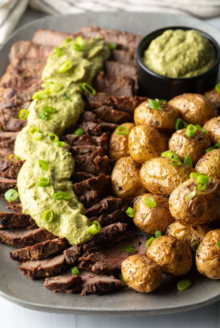 London Broil Marinade - London broil sliced into thick strips, covered with rich green sauce and chopped scallions with baby potatoes on the side.