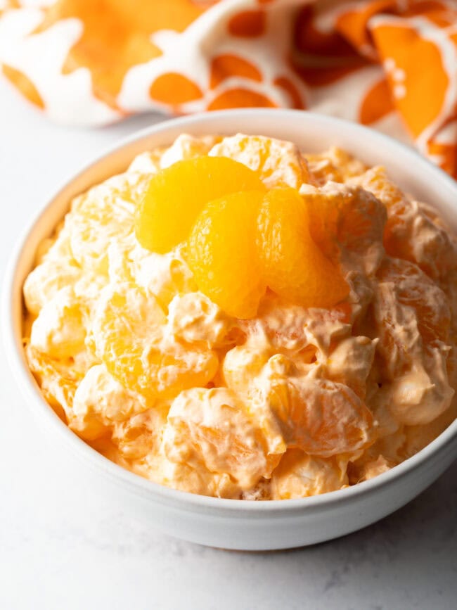 Top down view of orange fluff salad recipe in a white bowl, garnished with 3 slices of oranges.