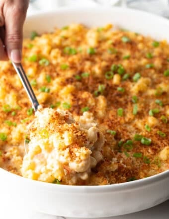 A spoon is scooping a serving of New Orleans style macaroni and cheese from a white dish.