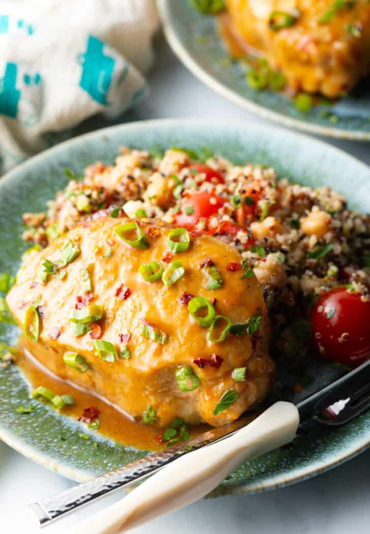 Baked pork chop covered with glaze and chopped scallions, on a plate next to quinoa salad with tomatoes.