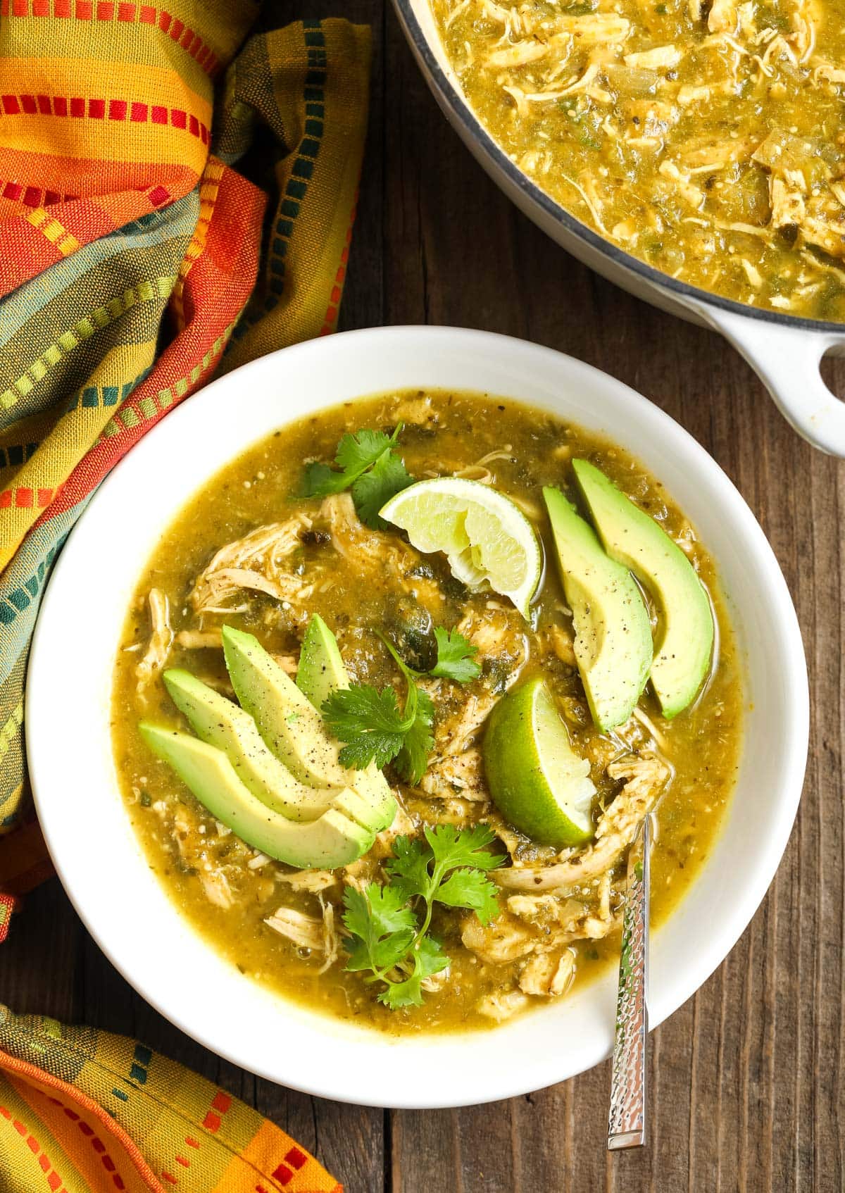 Top view of this chili verde in a bowl topped with some avocado and cilantro. 

