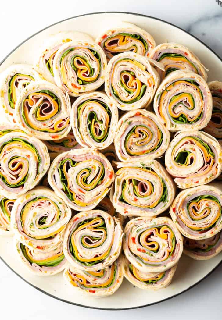 Two layers of a dozen pinwheels stacked on top of each other, on a white round plate.