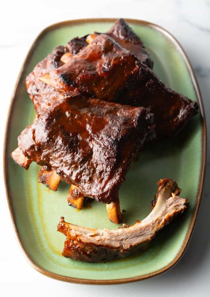 Three 4-piece sections and extra bone of slow cooker ribs on a green plate.