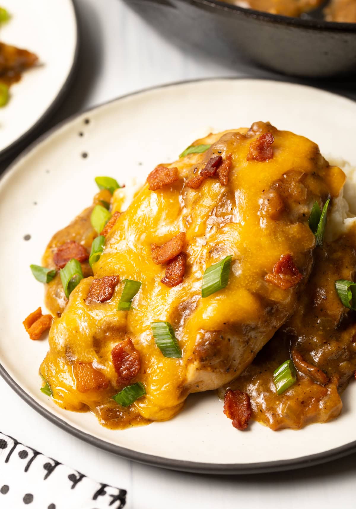 close up view of smothered chicken and gravy recipe with cheese, bacon, and scallions on a white plate.