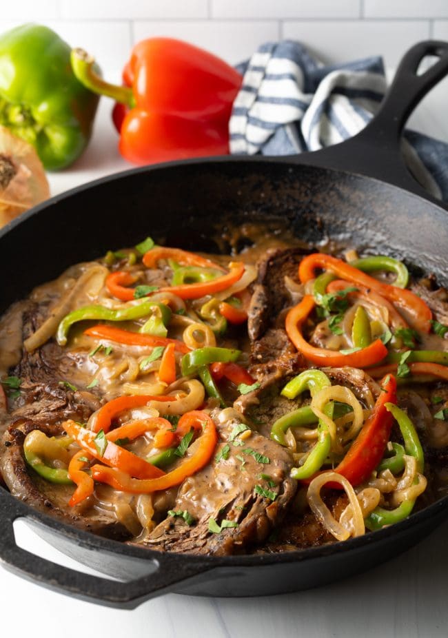 cast iron pan with steak, gravy, onions and peppers