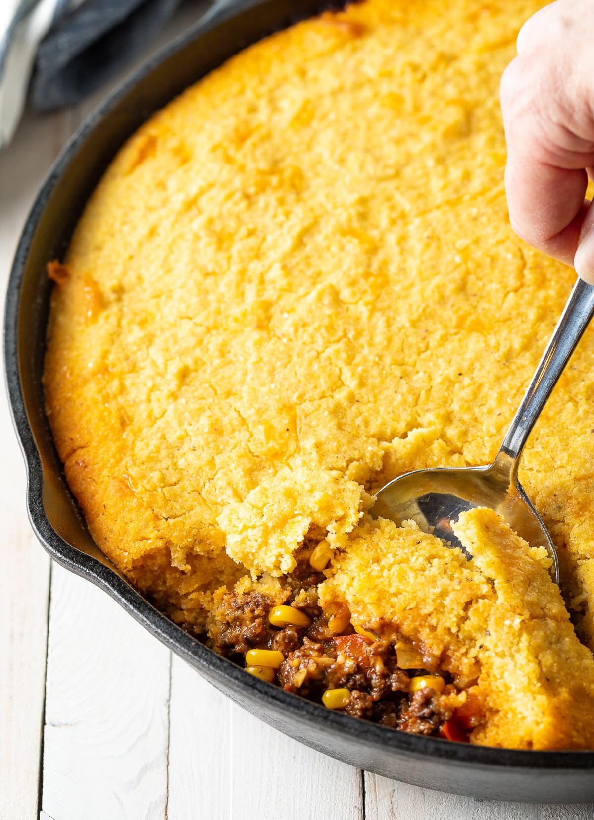 Tamale pie in a cast iron skillet with a spoon taking a portion. 