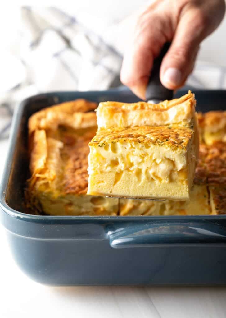 Hand removing a square of egg casserole with a spatula from a square baking dish.