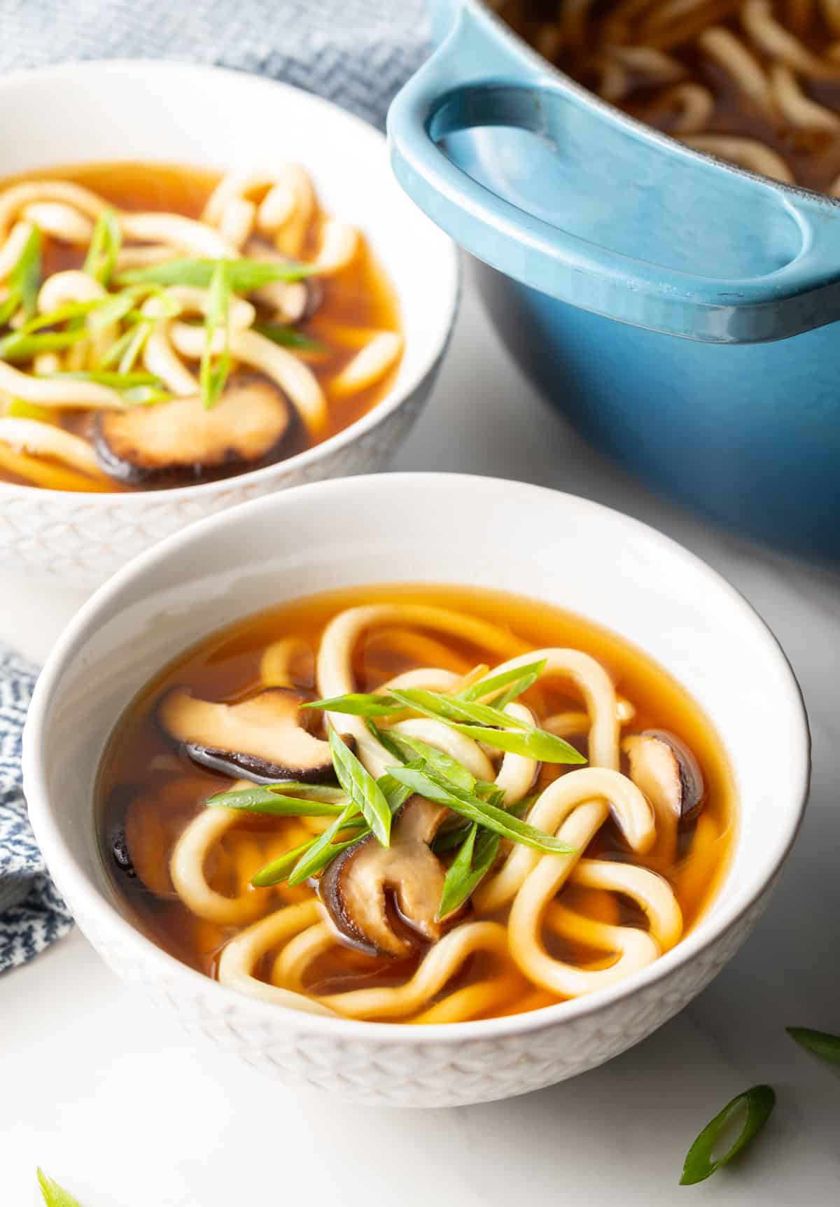 Easy udon noodle soup in 2 white bowls next to a pot of soup.