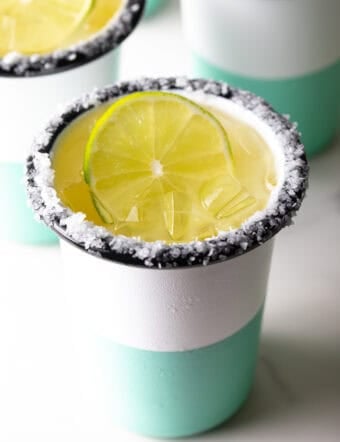 White and green-striped cup with salt around the rim and slice of lime in the drink.